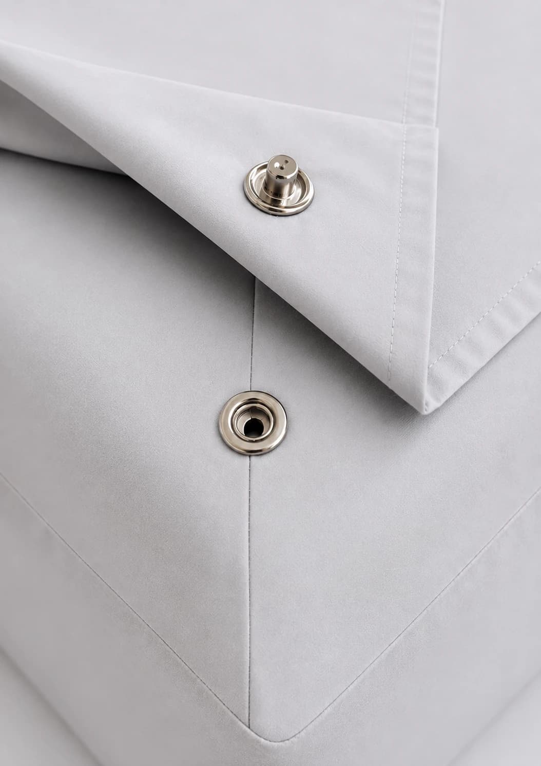 Close-up of the bottom sheet corner folded back, showing the snap fastener on the sheet and the matching snap on the fitted base below