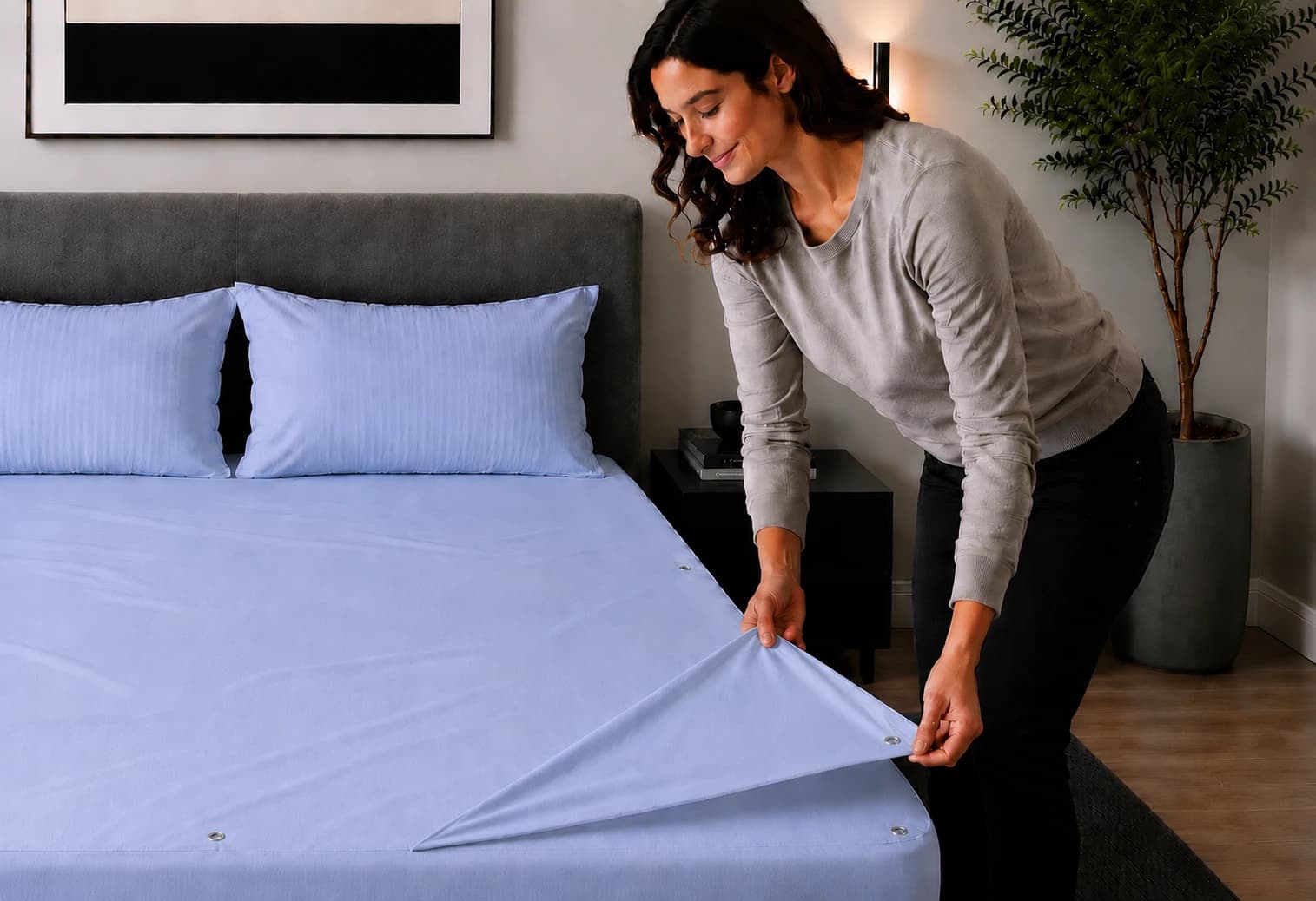 A woman lifting the corner of the light-blue bottom sheet away from the snap fasteners on the fitted base